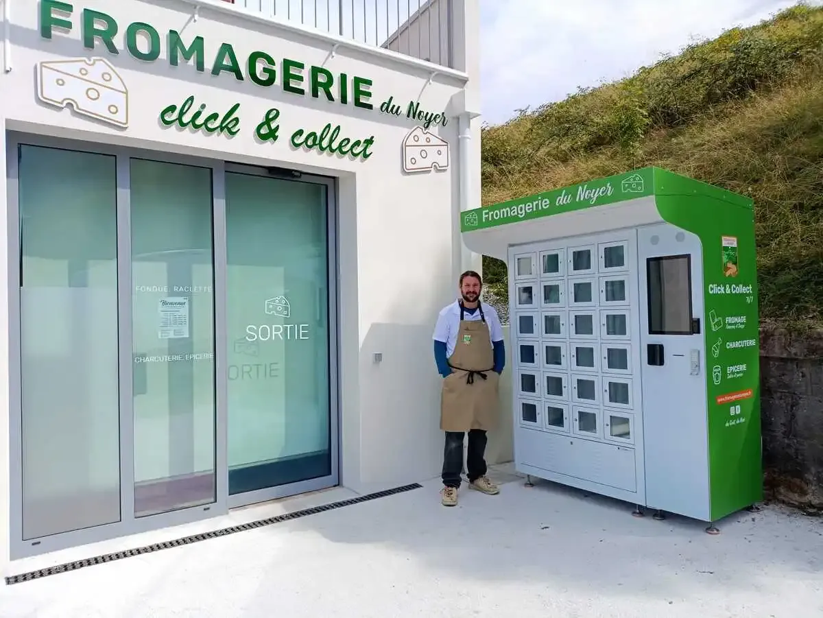 Photographie de Thibault Duval, gérant de la Fromagerie du Noyer, posant devant son distributeur automatique de fromages.